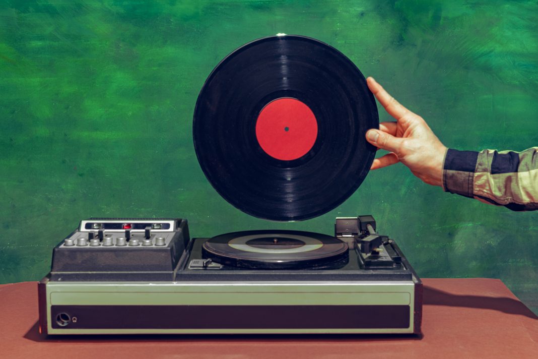 Colorful image of male hand holding retro vinyl record in front of vintage player isolated over dark green background